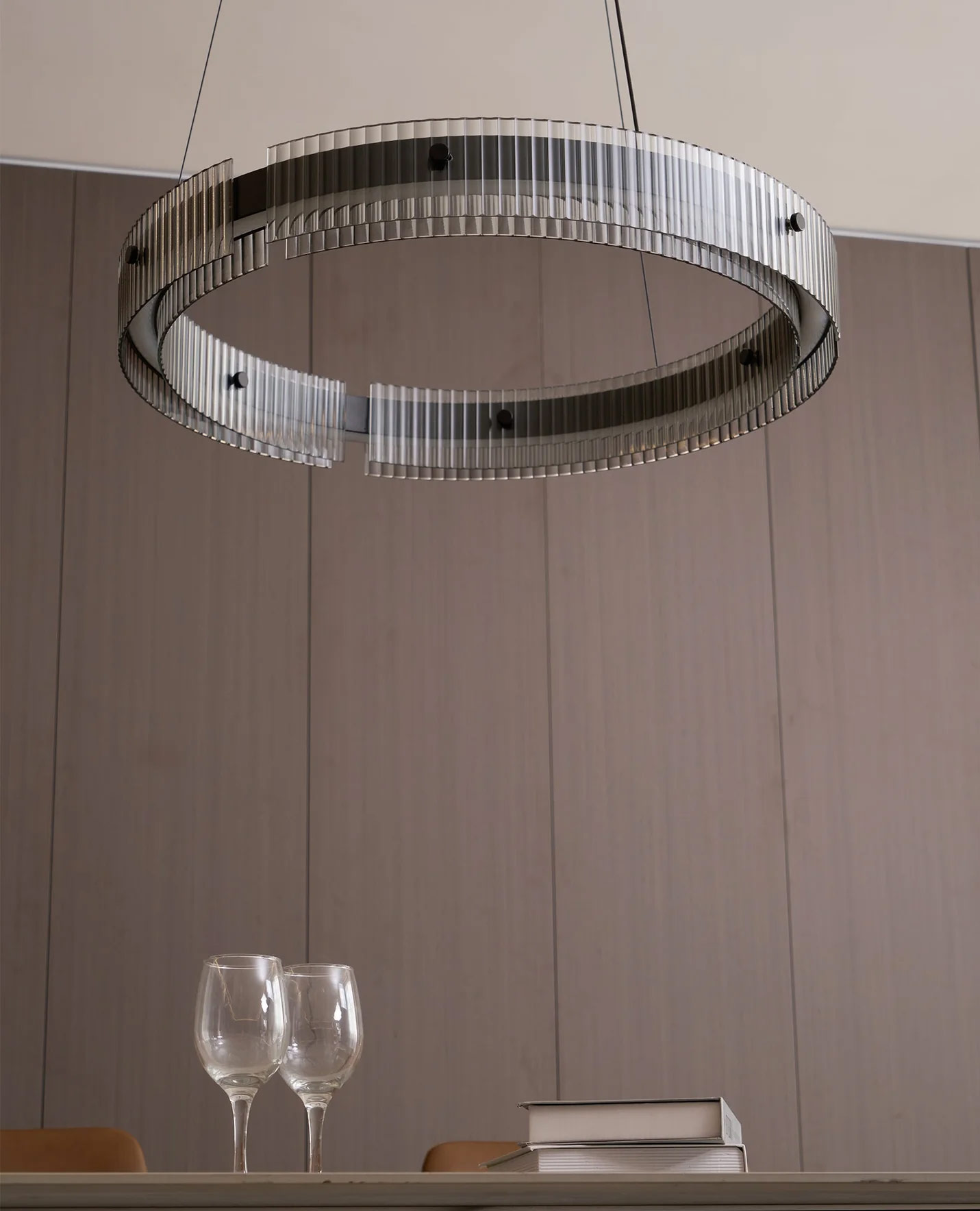 Modern circular pendant light with ribbed glass suspended over a dining table in a minimalist interior with dark fireplace and neutral walls
