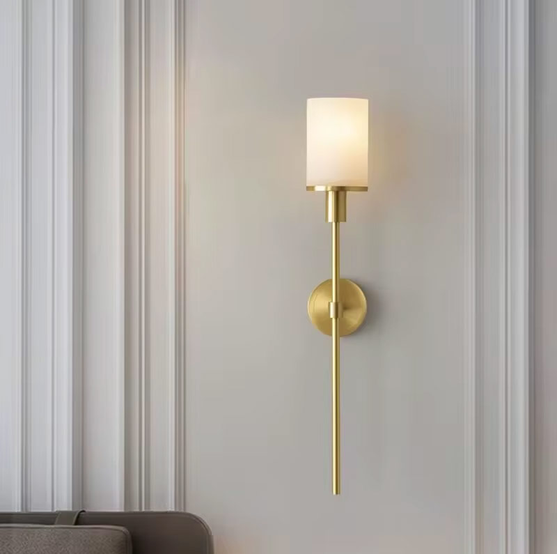 Vertical brass wall light with cylindrical alabaster shade in a living space
